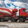 Red and white concrete mixer truck parked on rocky terrain under cloudy sky