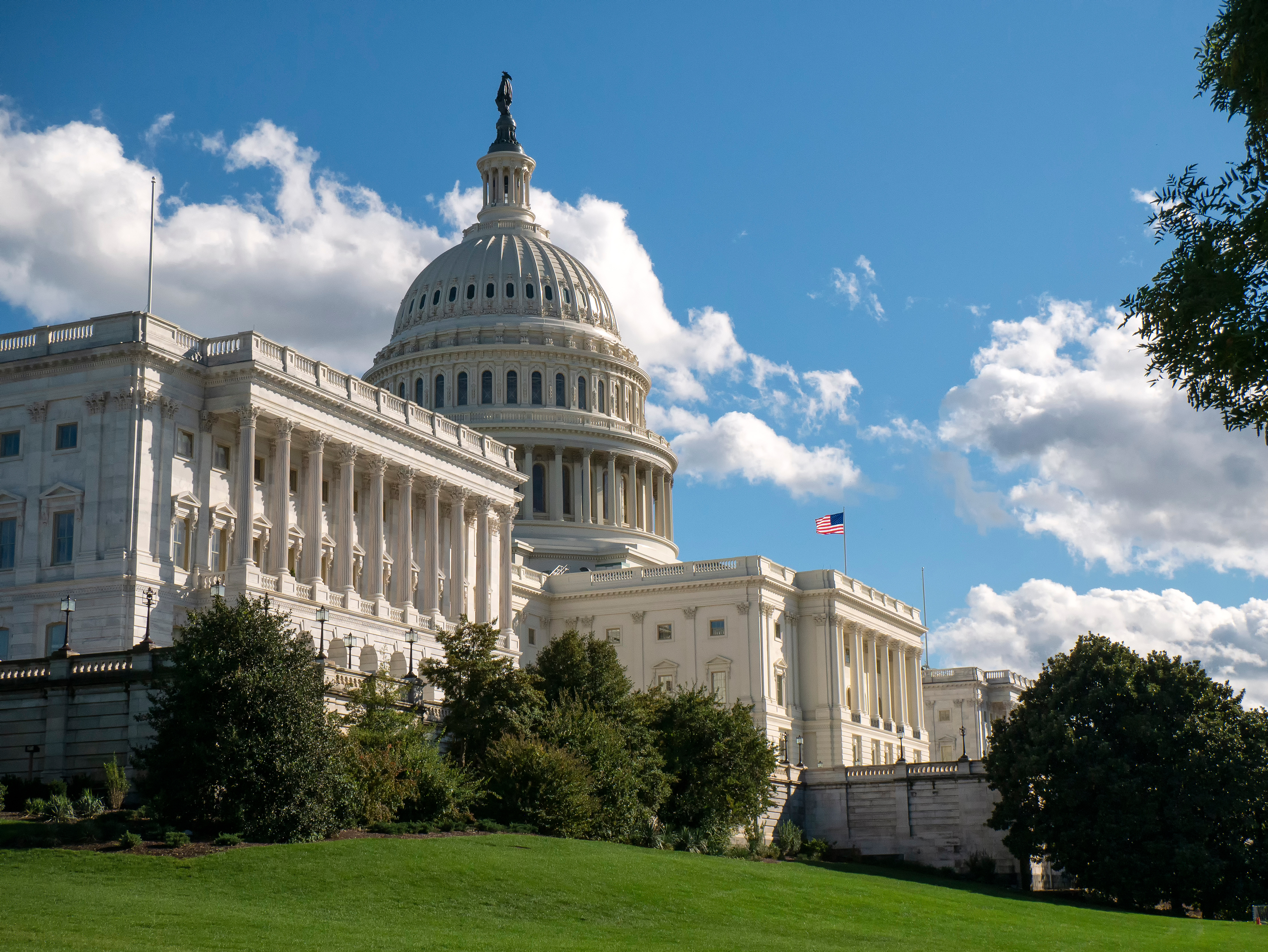 US Capitol building with white dome, columns, and American flag on clear blue sky day