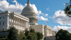 US Capitol building with white dome, columns, and American flag on clear blue sky day