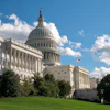 US Capitol building with white dome, columns, and American flag on clear blue sky day