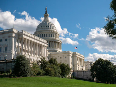 US Capitol building with white dome, columns, and American flag on clear blue sky day