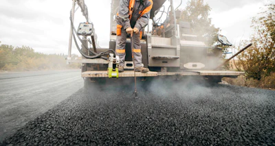 Road construction worker operating asphalt paving machine laying fresh black tarmac