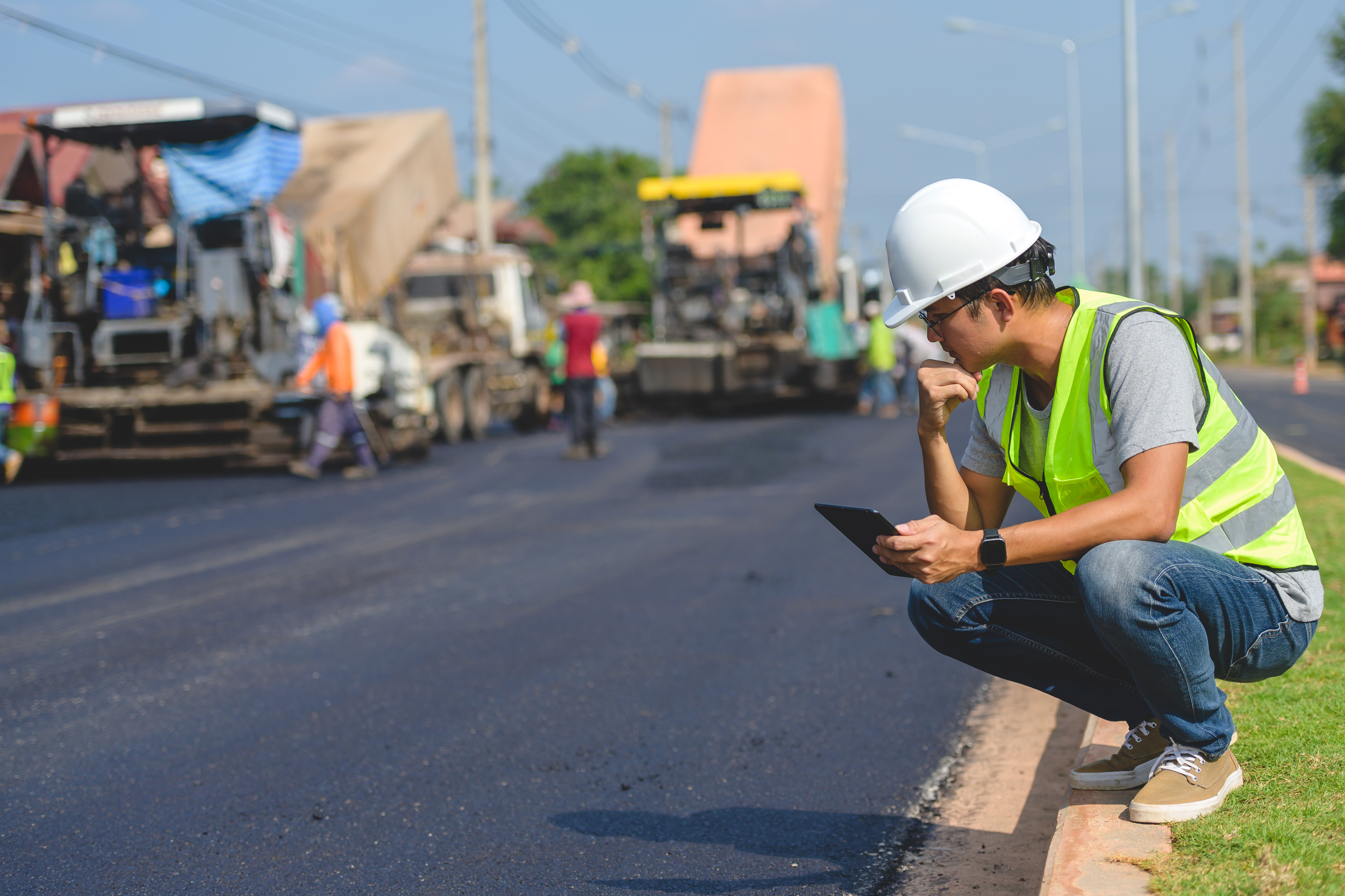 Construction worker in safety vest reviewing plans on roadside during asphalt paving project