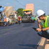 Construction worker in safety vest reviewing plans on roadside during asphalt paving project