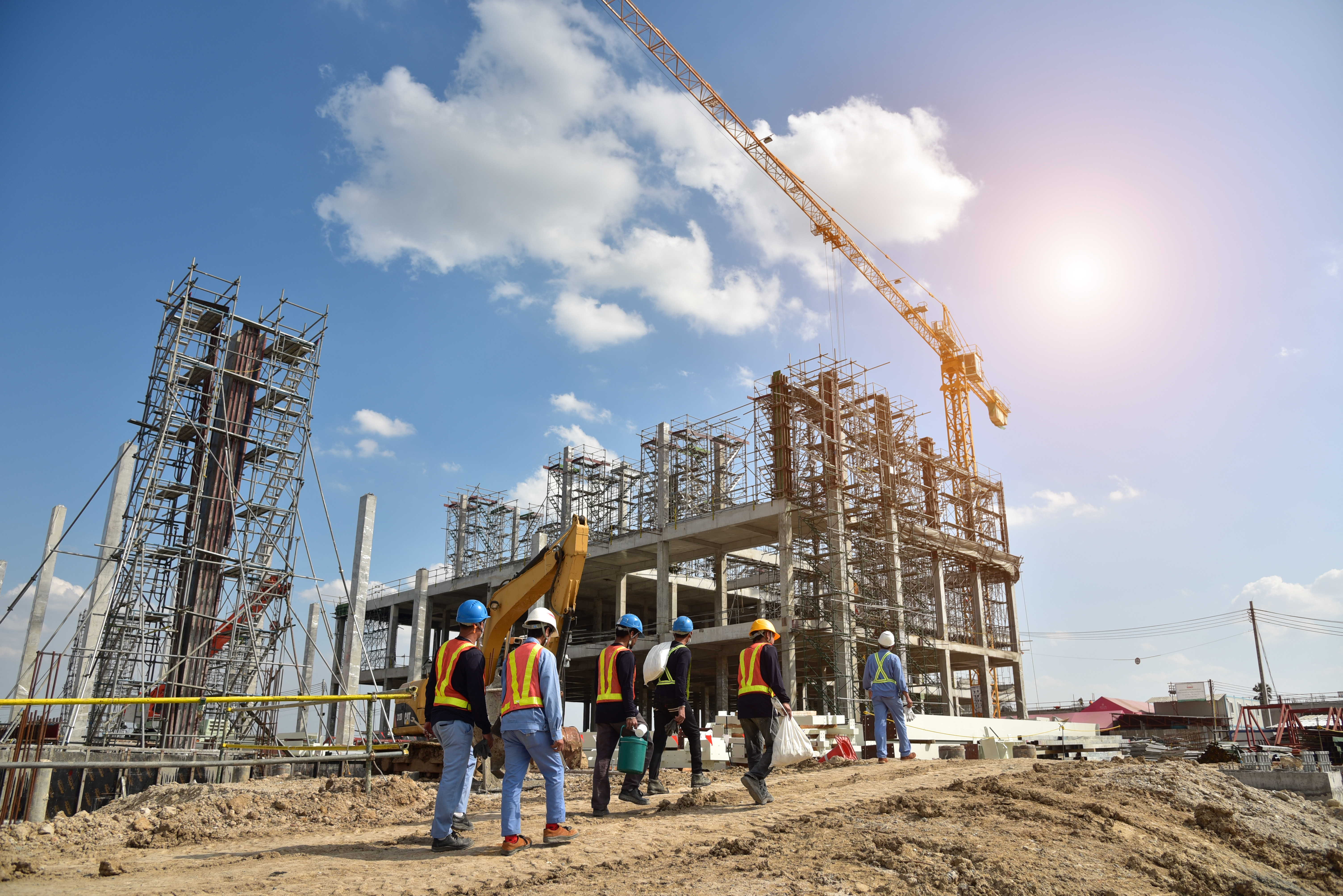 Construction workers in safety gear observing building progress with steel framework and crane against blue sky