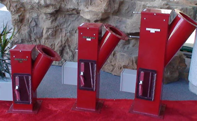 Three red industrial machines with angled metal components on gray stone surface