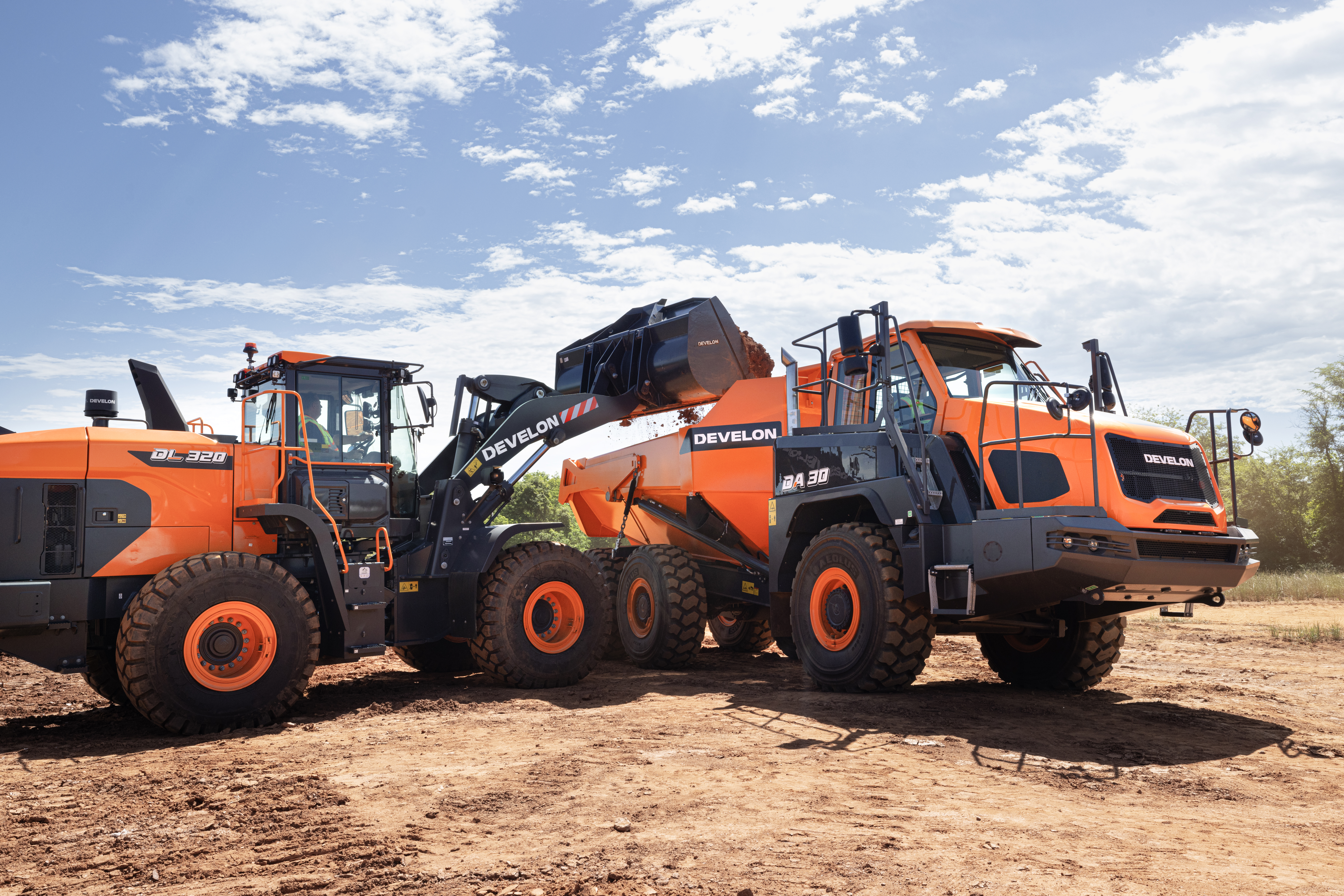 Three orange Develon construction vehicles parked on dirt at a worksite