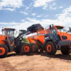 Three orange Develon construction vehicles parked on dirt at a worksite