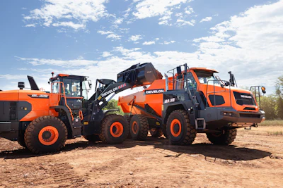 Three orange Develon construction vehicles parked on dirt at a worksite