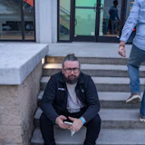 PAVEX team member sitting on concrete steps, wearing black jacket and glasses