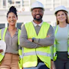 Three construction workers in safety vests and hard hats smiling on job site