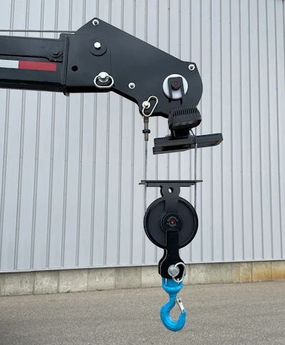 Black industrial crane mechanism with blue hook against metal wall