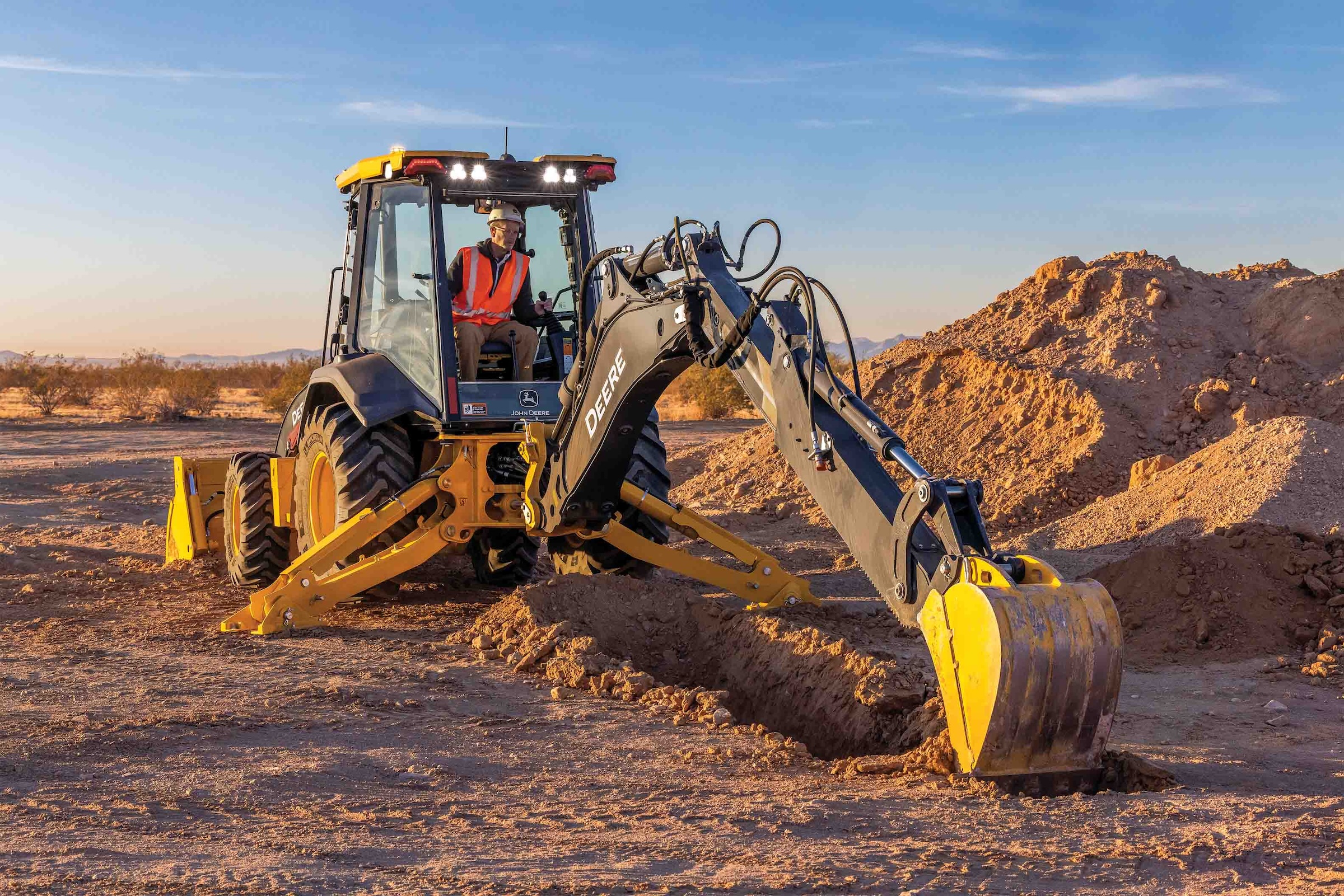 Yellow John Deere backhoe digging trench in arid desert construction site