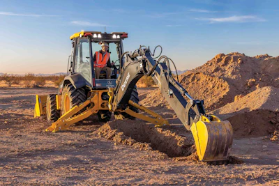 Yellow John Deere backhoe digging trench in arid desert construction site