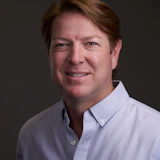Professional headshot of a smiling man in a white button-down shirt