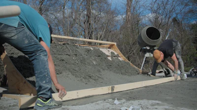 Construction workers leveling wet concrete with wooden forms on site