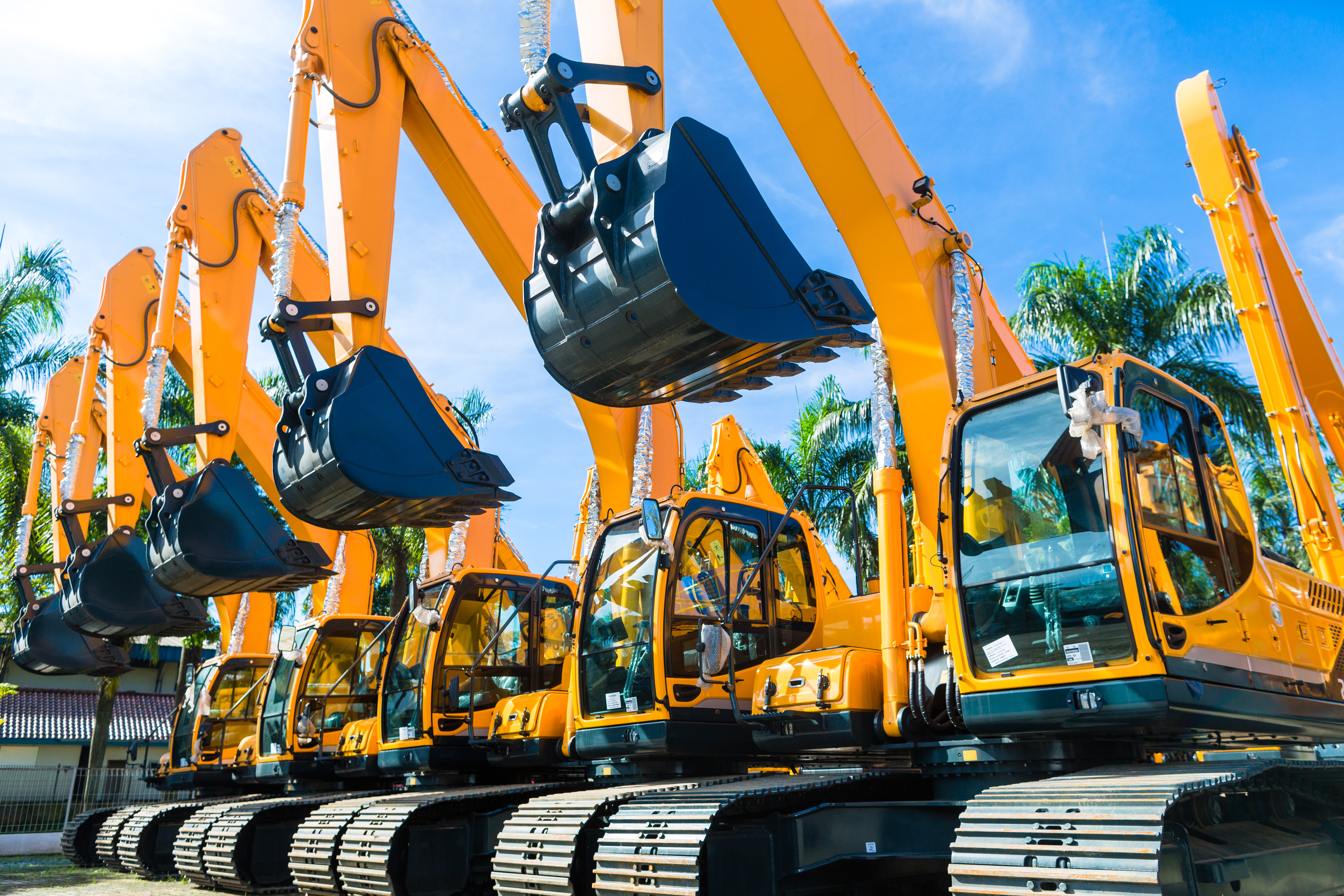 Fleet of bright orange hydraulic excavators lined up with palm trees