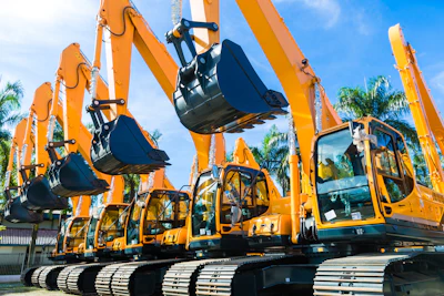 Fleet of bright orange hydraulic excavators lined up with palm trees