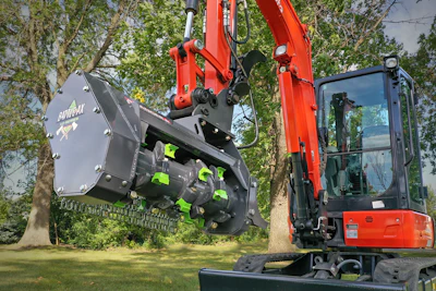 Red compact excavator with forestry mulching attachment clearing vegetation near trees