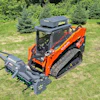 Orange Kubota skid steer loader with forestry mulcher attachment on grassy field