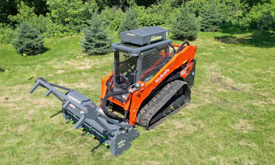 Orange Kubota skid steer loader with forestry mulcher attachment on grassy field