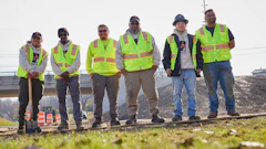 Six construction workers in bright safety vests standing on railroad tracks