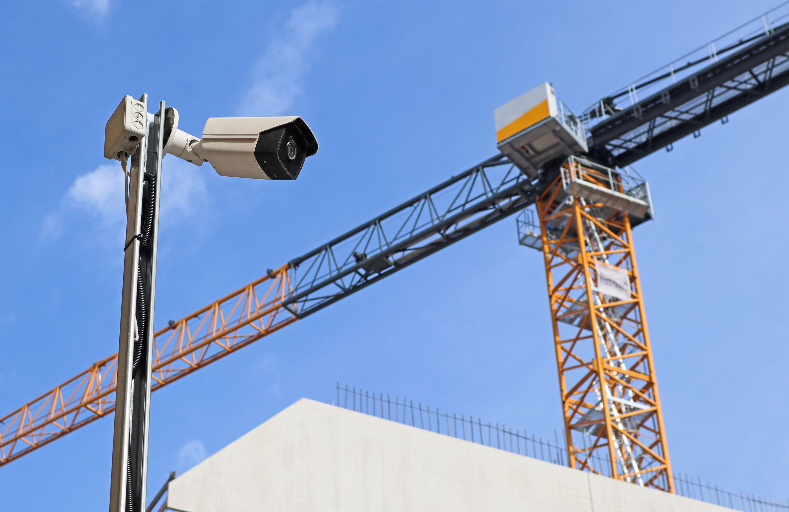 Security camera overlooking yellow construction crane against blue sky