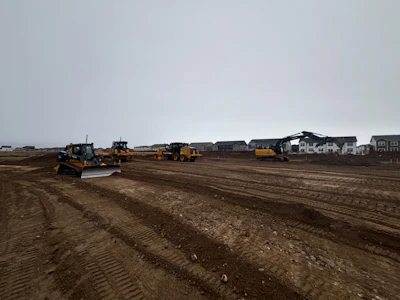Construction site with yellow excavators and bulldozers preparing land near new housing development