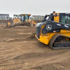 Yellow John Deere construction vehicles working on dirt lot near residential development