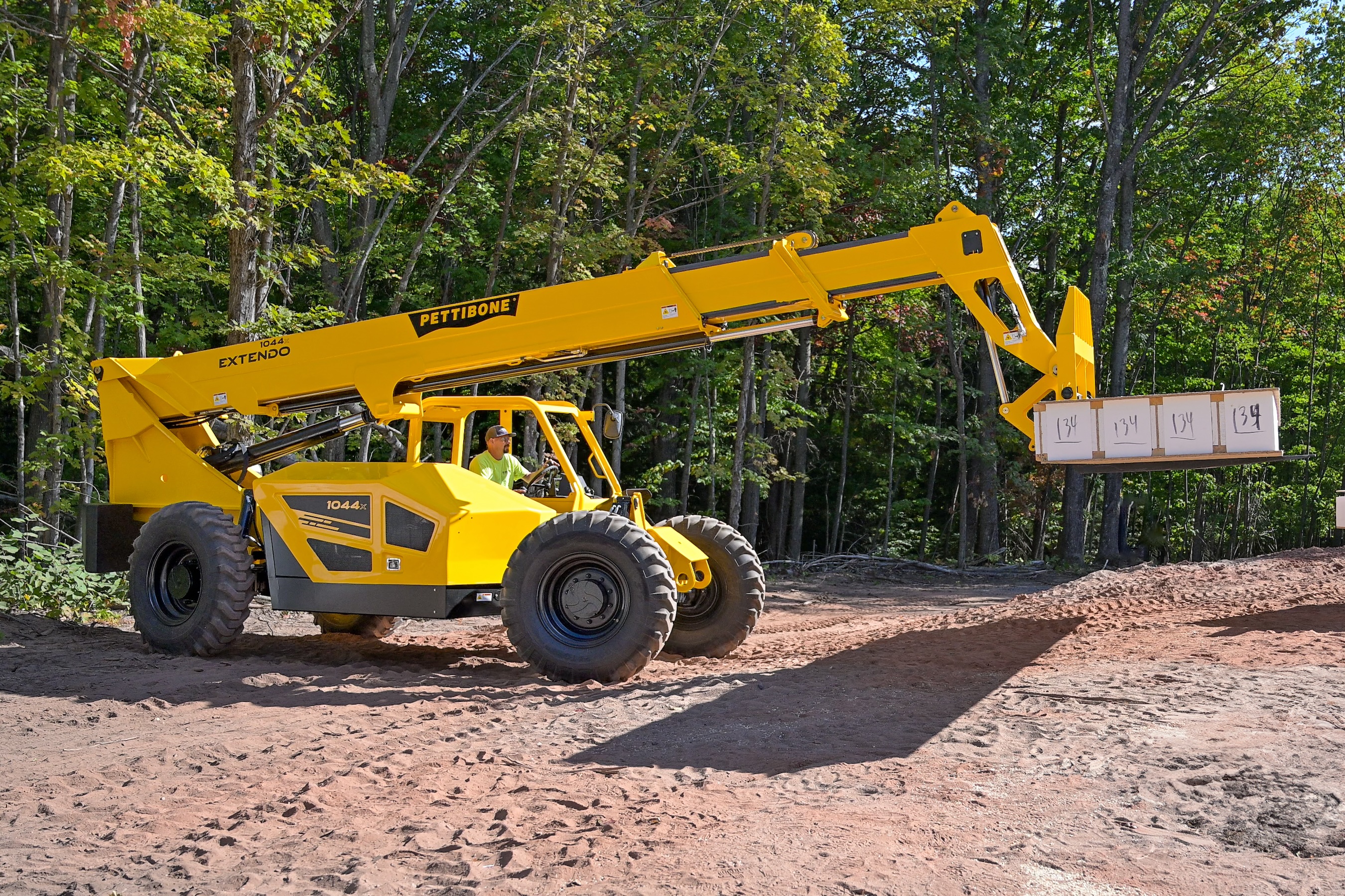 Yellow Pettibone telehandler on dirt path surrounded by trees