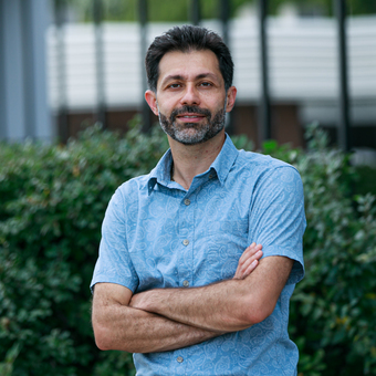 Professional man in blue shirt standing confidently outdoors near greenery Headshot