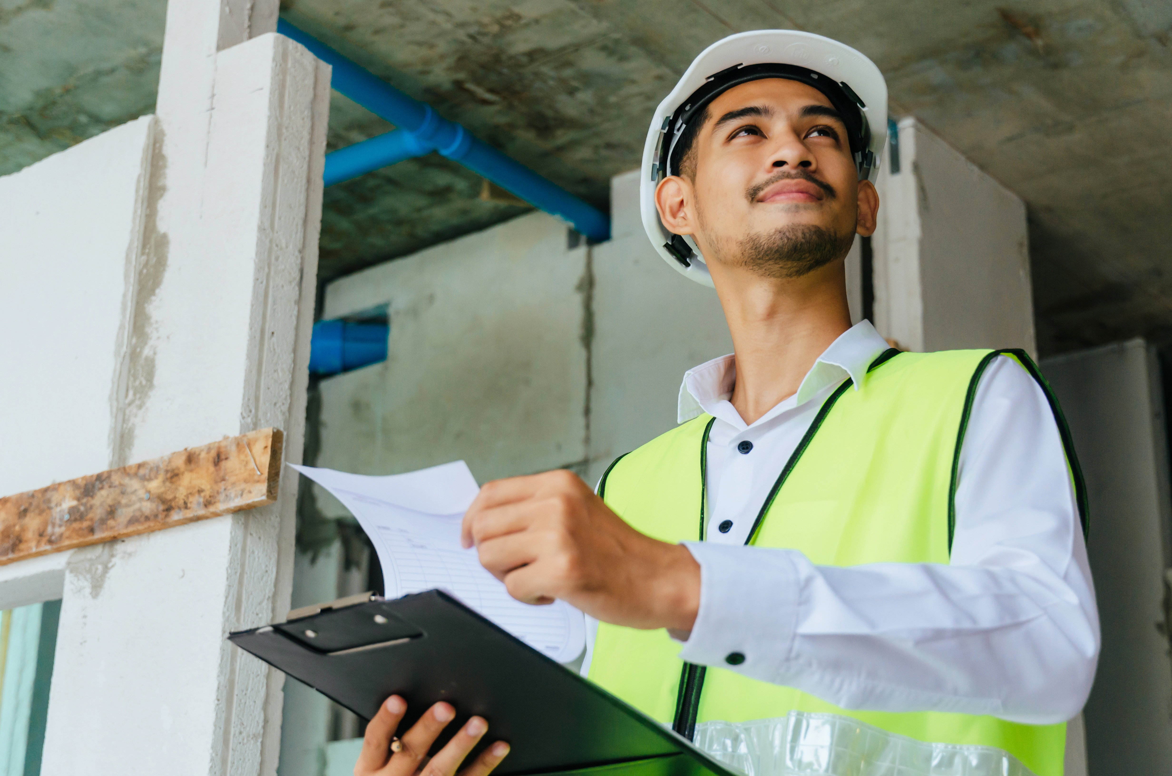 Construction worker in white hard hat and yellow safety vest reviewing documents on site