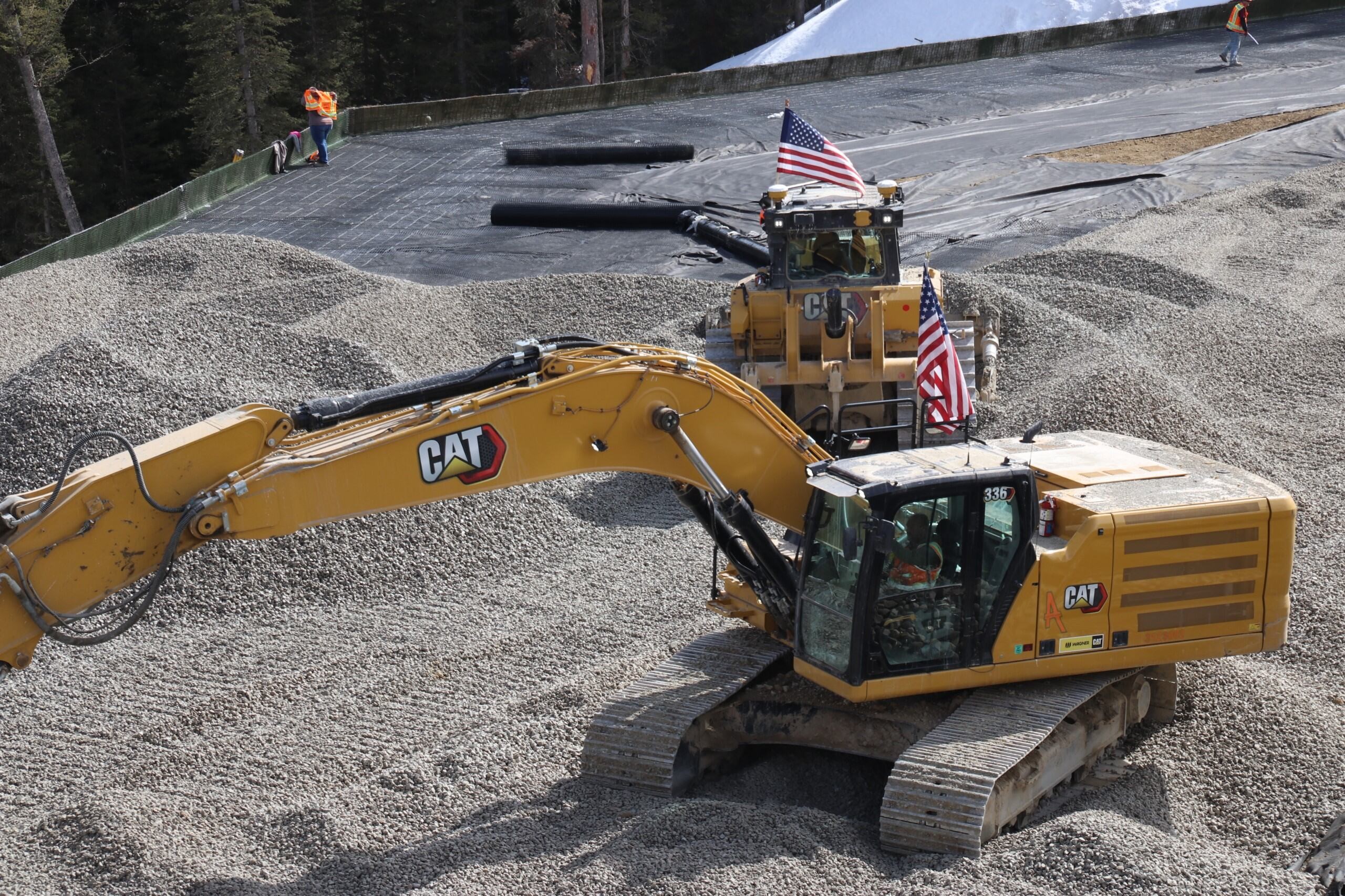 Yellow Caterpillar excavator with American flags at construction site with gravel