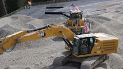 Yellow Caterpillar excavator with American flags at construction site with gravel