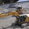 Yellow Caterpillar excavator with American flags at construction site with gravel