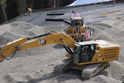 Yellow Caterpillar excavator with American flags at construction site with gravel