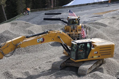 Yellow Caterpillar excavator with American flags at construction site with gravel