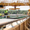 Construction workers installing concrete panels using overhead crane at infrastructure site