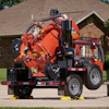 Red industrial vacuum truck trailer parked on concrete with brick house in background