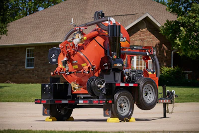 Red industrial vacuum truck trailer parked on concrete with brick house in background