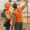 Two construction workers in orange safety vests surveying a construction site