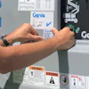 Hands placing or checking a QR code on Genie equipment panel with multiple warning labels and safety instructions