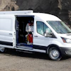 White Ford Transit cargo van with side door open, parked on rocky ground