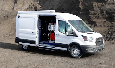 White Ford Transit cargo van with side door open, parked on rocky ground