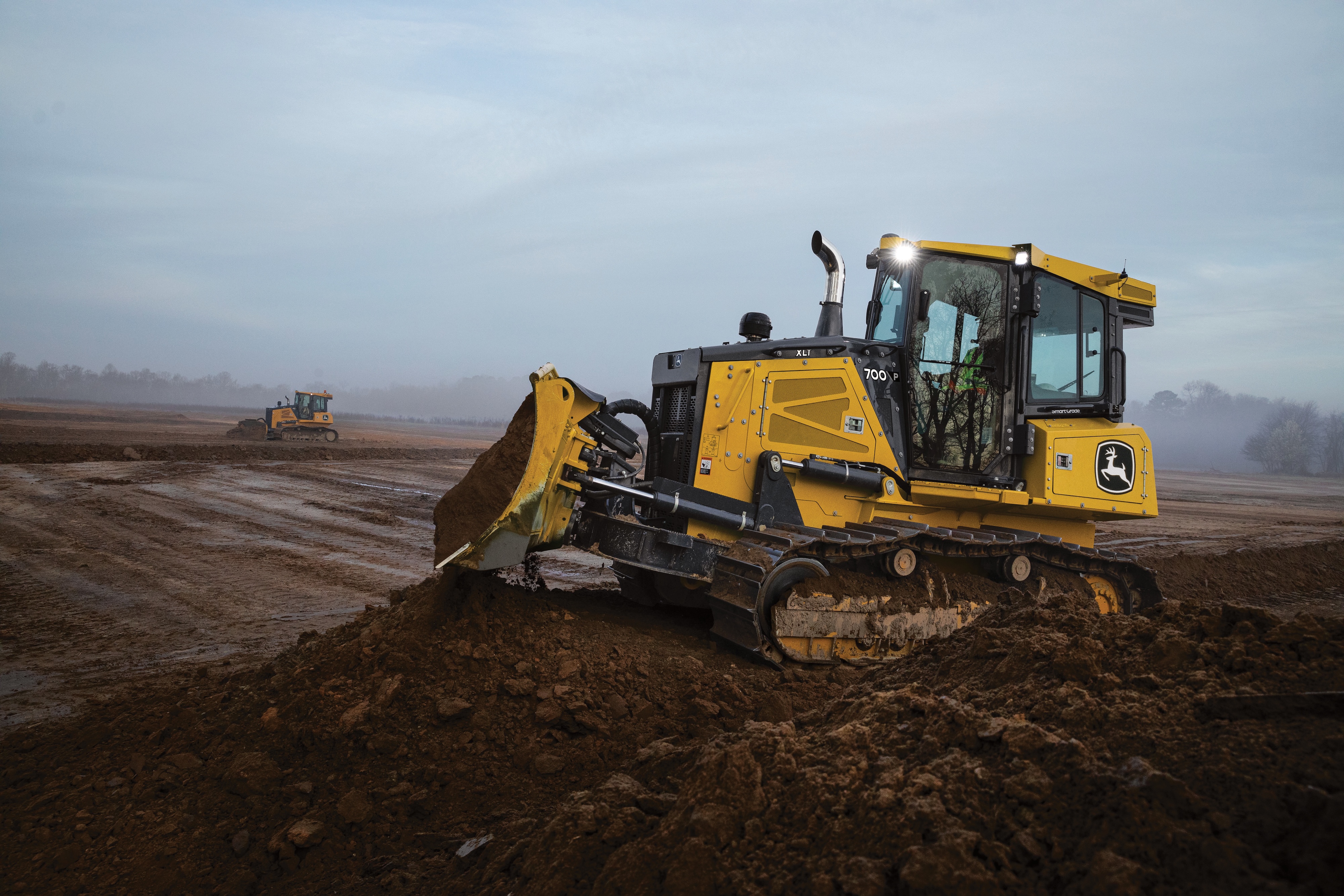 Yellow John Deere bulldozer moving earth on a construction site at dawn