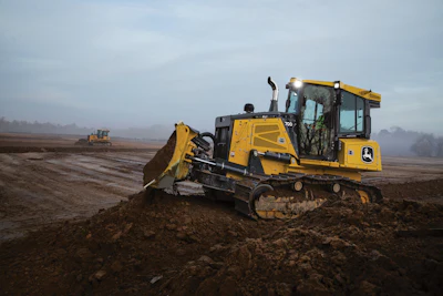 Yellow John Deere bulldozer moving earth on a construction site at dawn