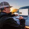 Mature worker using laptop on truck hood at golden hour sunset