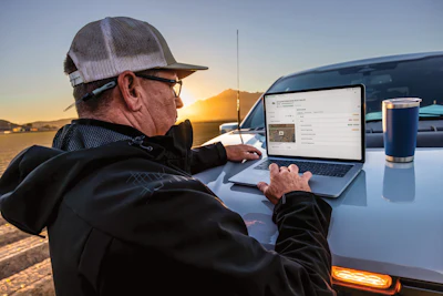 Mature worker using laptop on truck hood at golden hour sunset