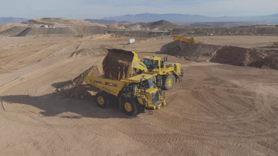 Yellow mining haul truck moving earth in desert quarry with mountain landscape