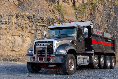 Gray Mack dump truck parked in rocky quarry with stone cliff background